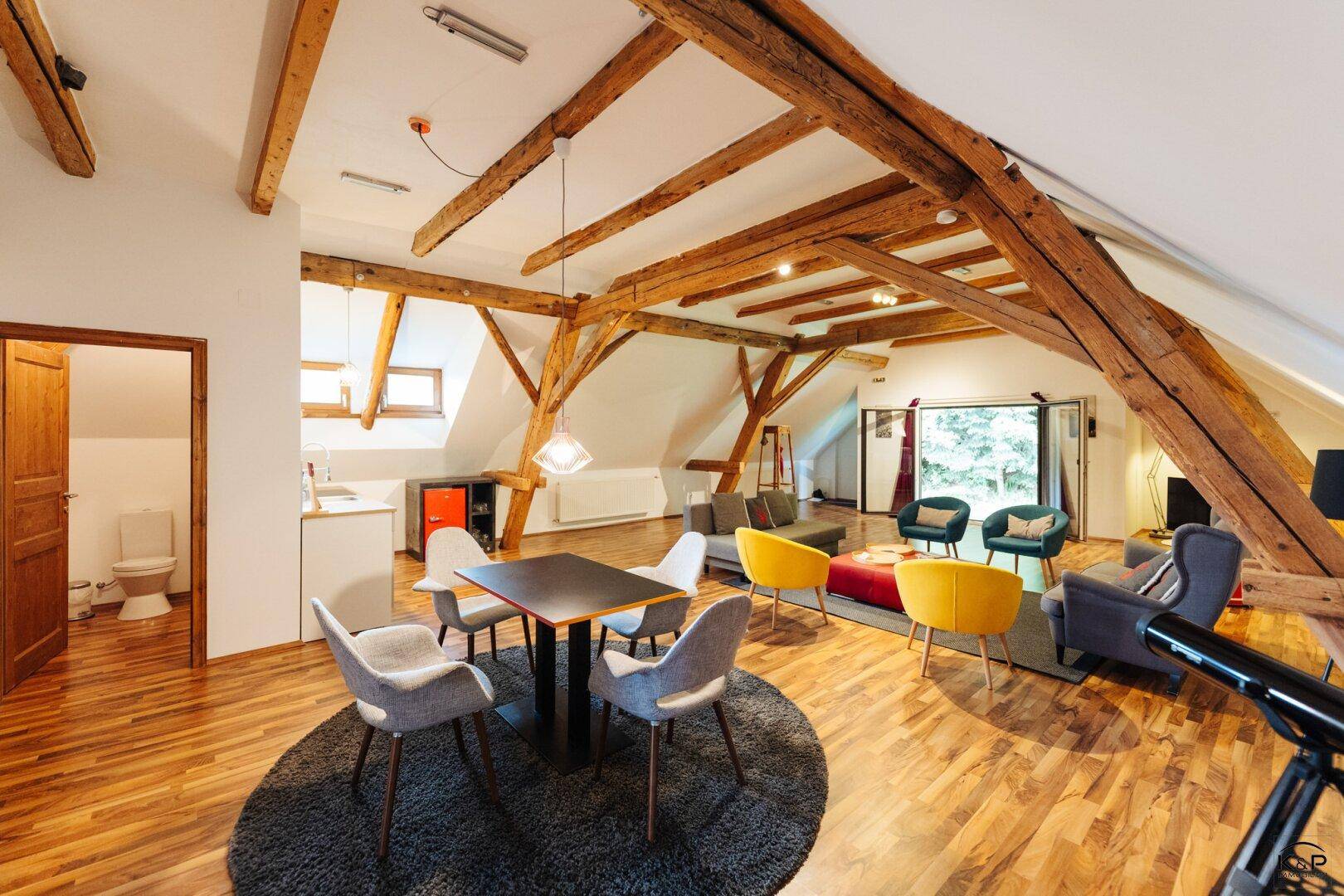 Offener Wohn- und Essbereich im Dachgeschoss mit freiliegenden Holzbalken und moderner Einrichtung.