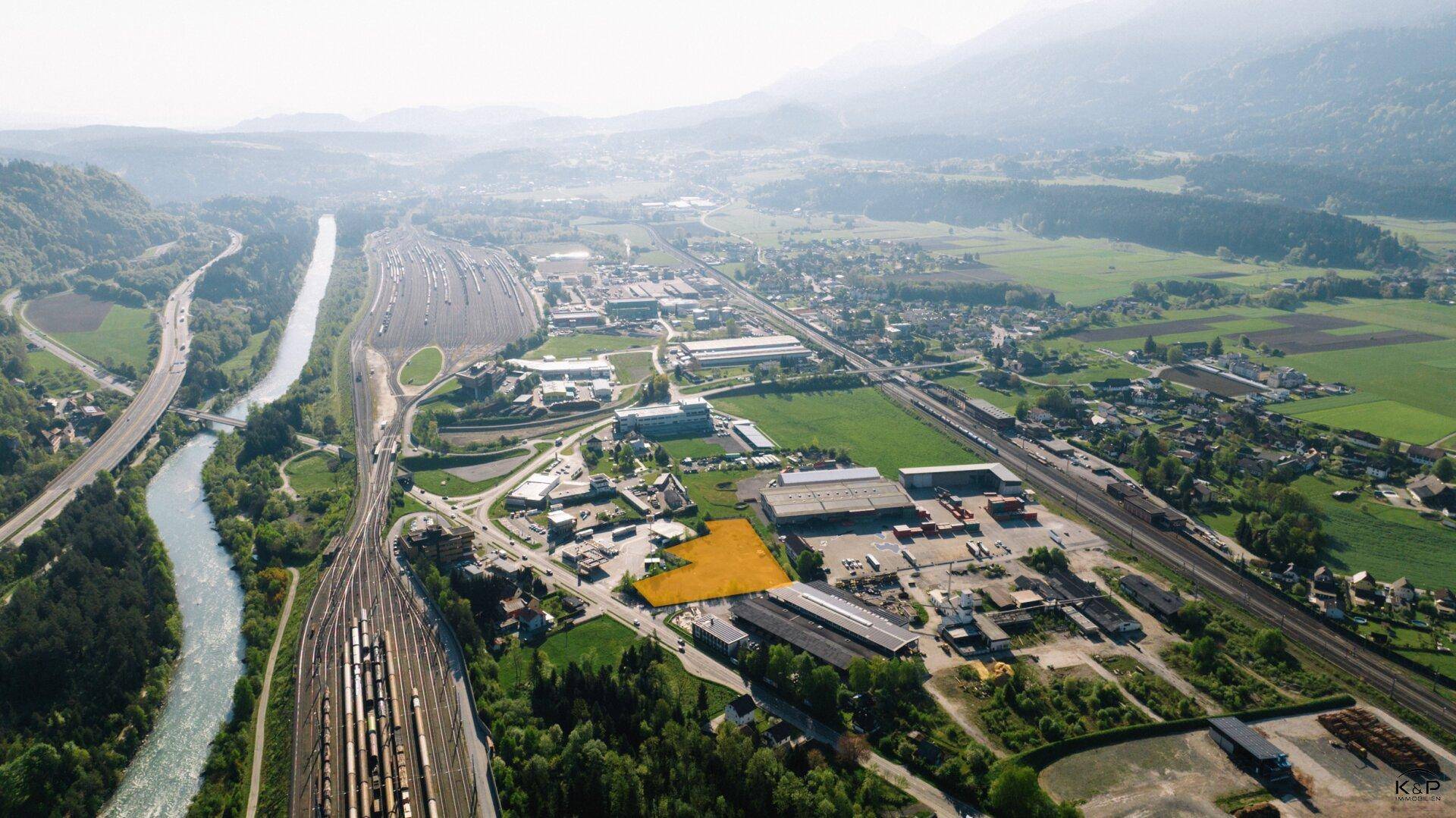 Weitwinkel-Luftaufnahme eines Grundstücks in einer Industriezone mit Bergen, Fluss und Bahnlinien.