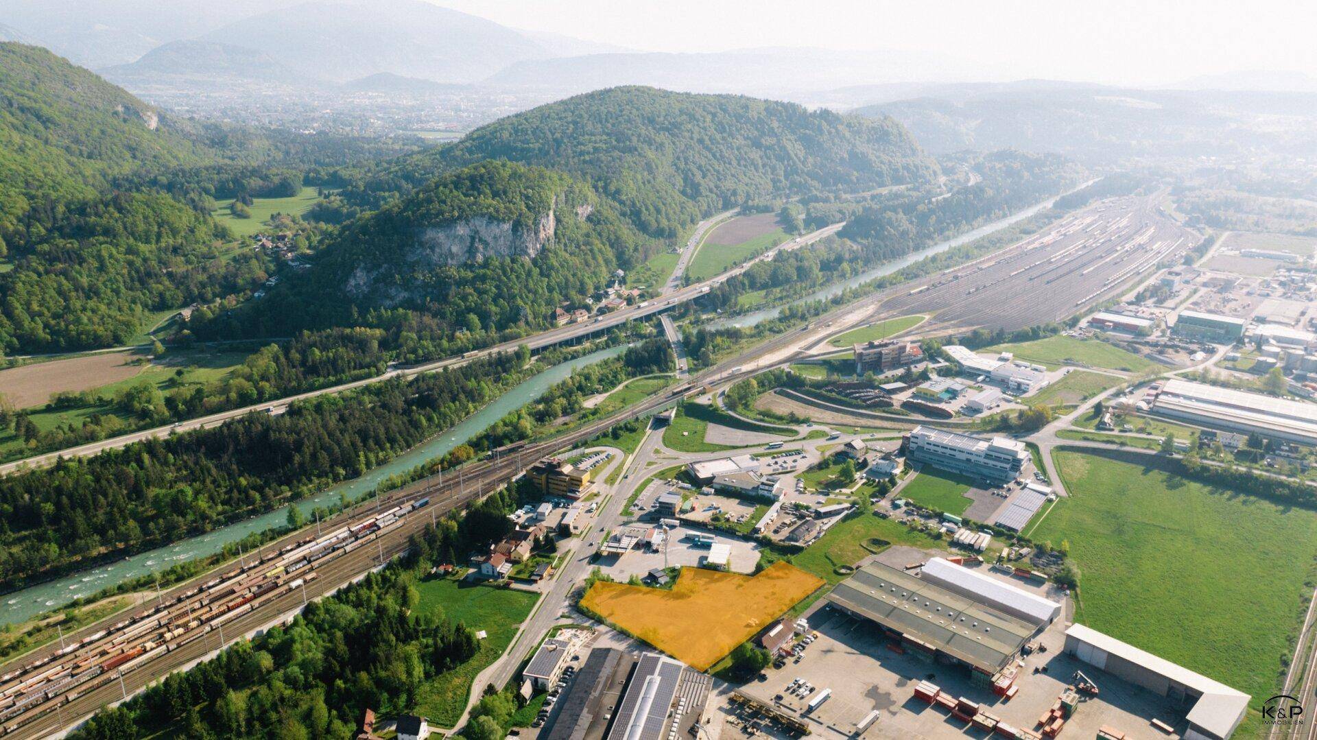 Panoramablick auf ein Grundstück in einer Industriezone, umgeben von Bergen und einem Flusslauf.