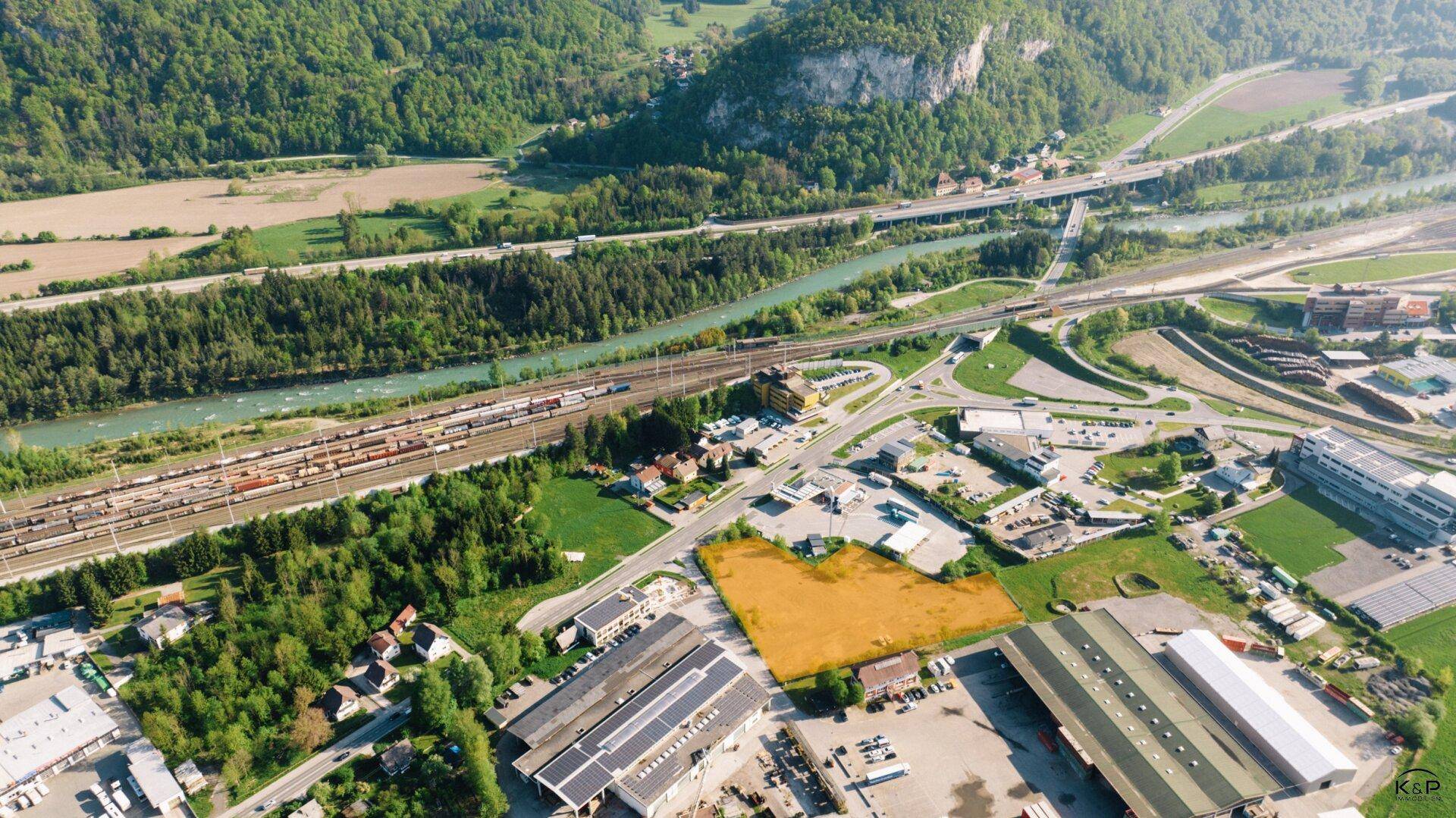 Luftaufnahme eines Grundstücks in einer Industriezone mit Bergen, Fluss und Autobahn im Hintergrund.