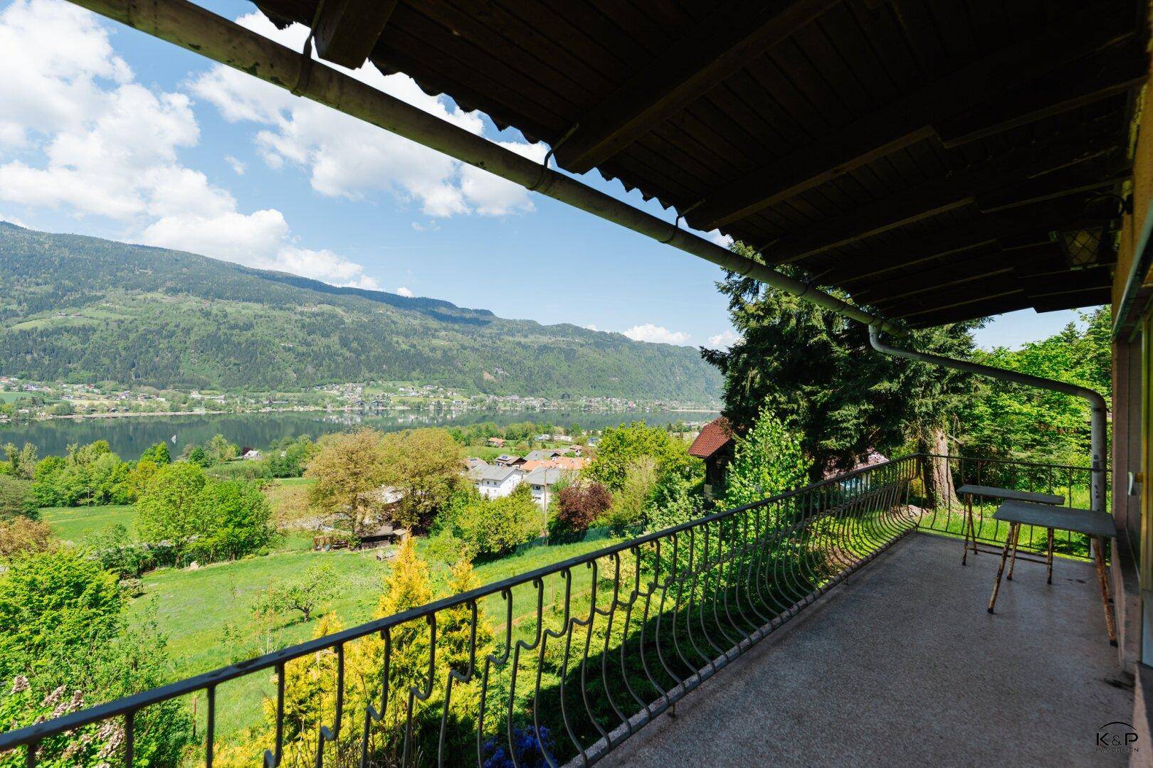 Langer Balkon mit Metallgeländer und weitem Blick über einen See und die umliegende Natur.