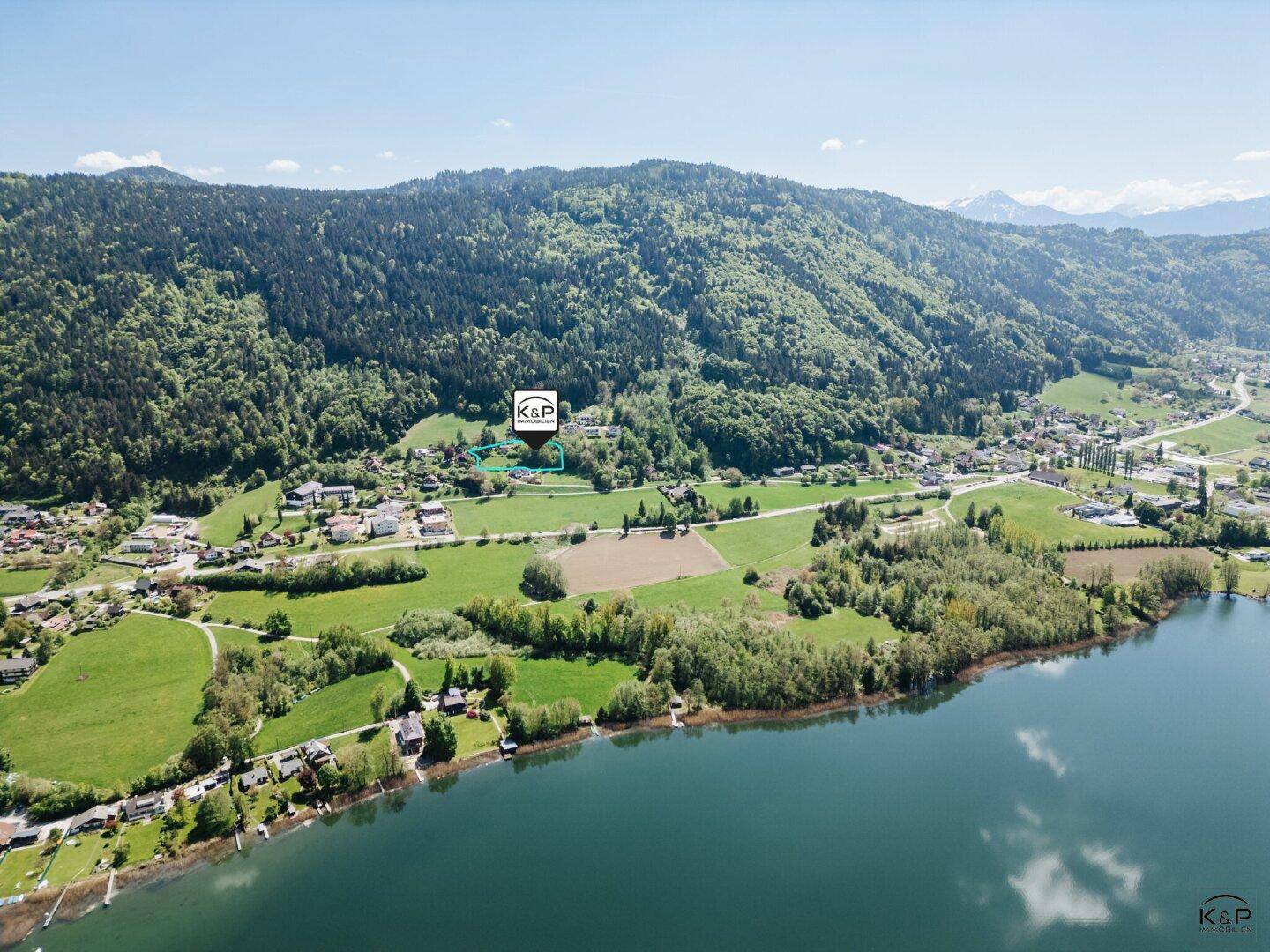 Luftaufnahme der Umgebung mit einem See, grünen Feldern und einem markierten Grundstück in der Landschaft.
