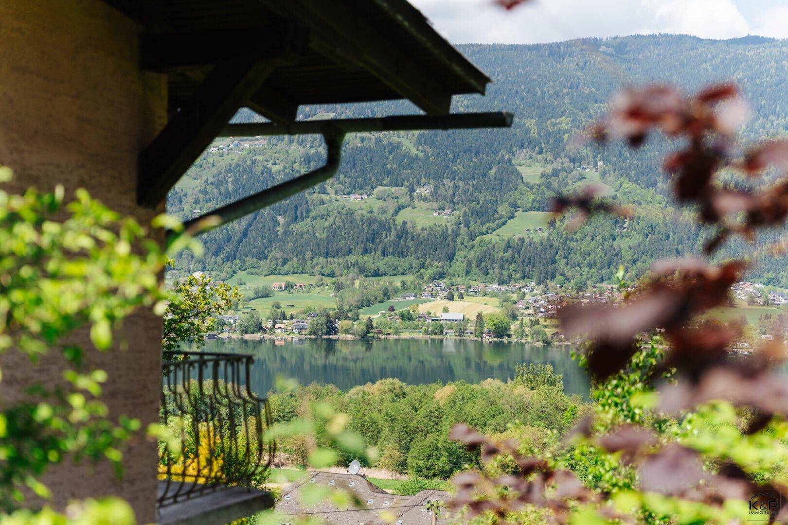 Aussicht von einem Balkon mit schmiedeeisernem Geländer auf einen See und die umliegende grüne Natur.