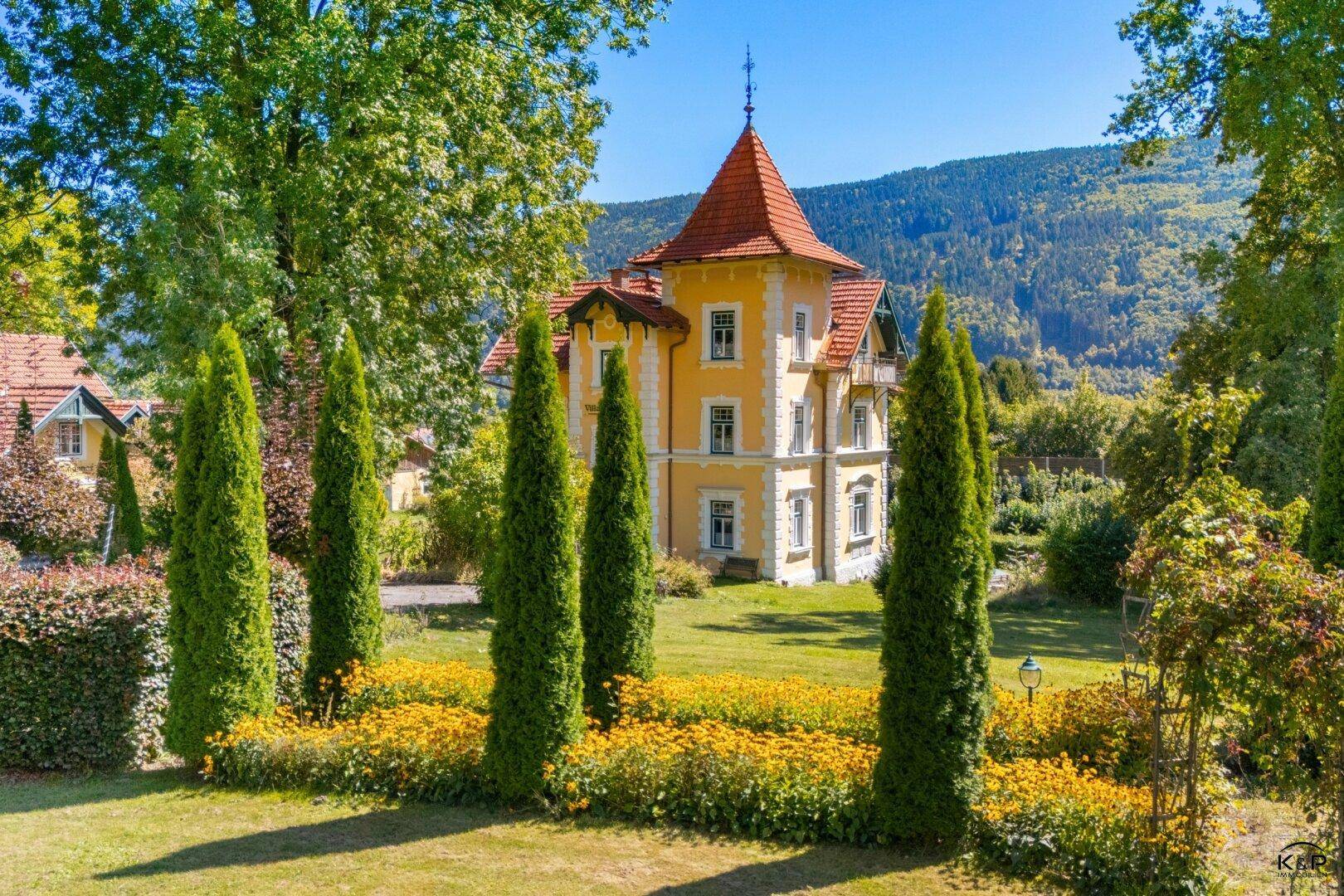 Malerischer Gartenbereich mit Zypressen und blühenden Blumenbeeten vor der historischen Villa.