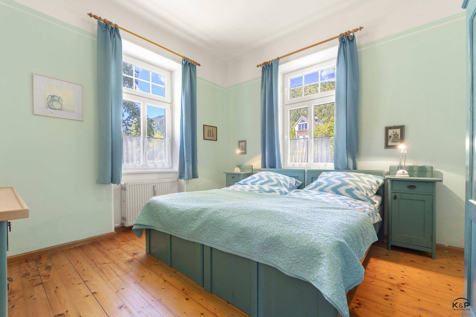 Helles Schlafzimmer mit Holzboden, hellgrünen Wänden und Fenstern mit Bergblick.