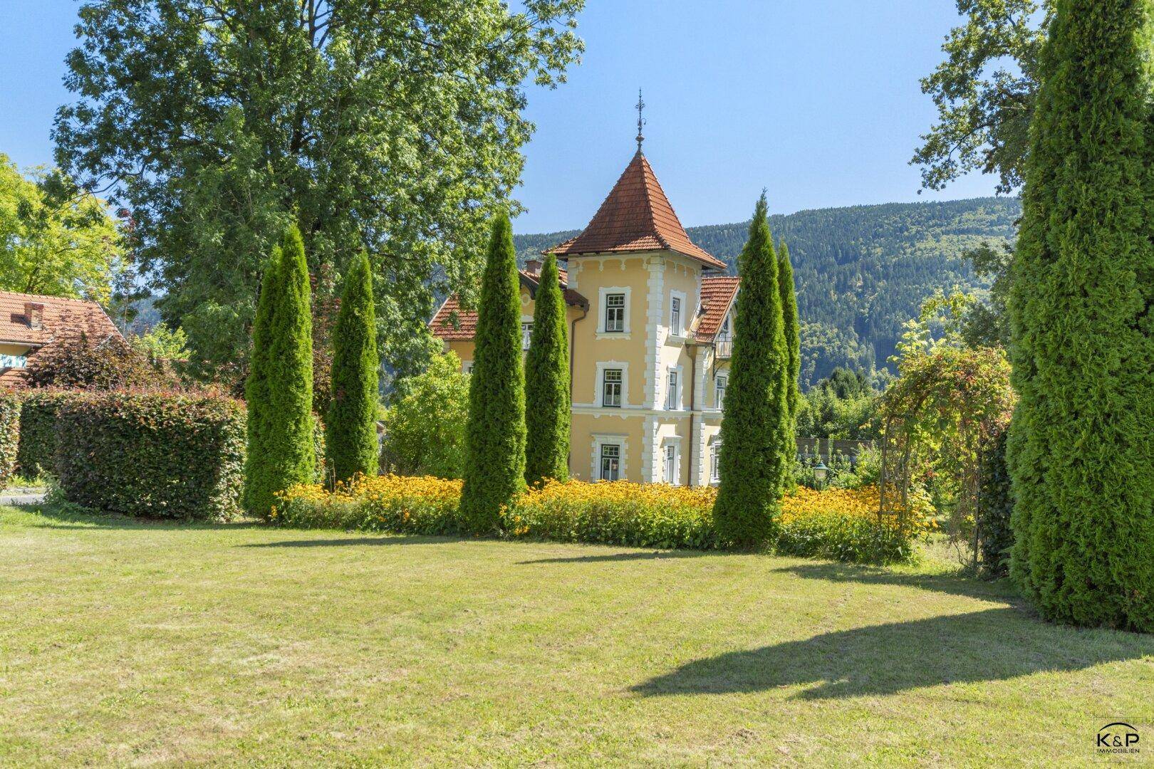 Weitläufiger Rasenbereich im Garten mit Blick auf die historische Villa und die umliegende Natur.