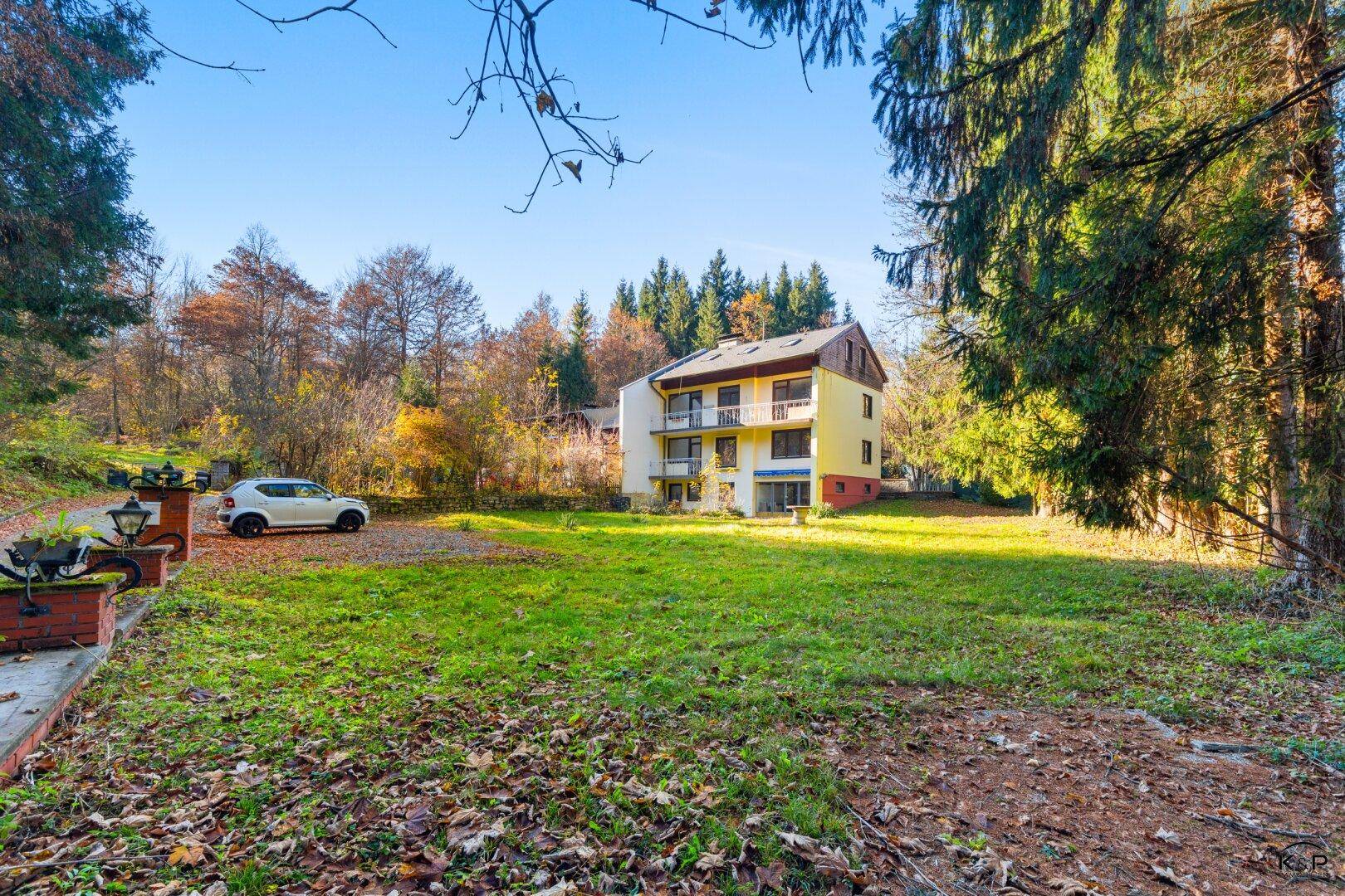 Geräumiger Gartenbereich mit Rasenfläche und Blick auf das Mehrfamilienhaus umgeben von Bäumen.