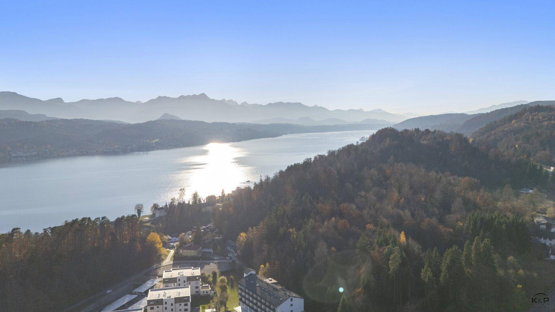 Weitläufiger Panoramablick auf einen See, umgeben von Bergen und einer Siedlung am Ufer.