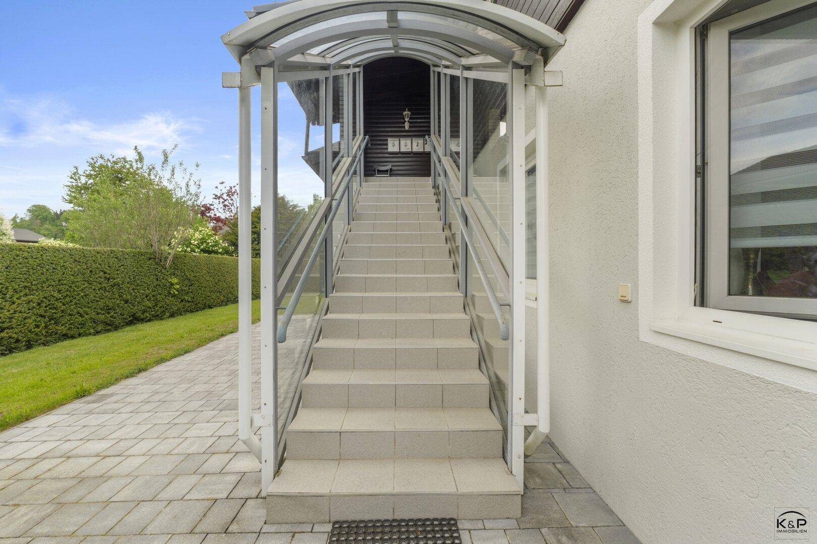 Überdachte Außentreppe mit Glasgeländer, die zum Eingang des Hauses führt.