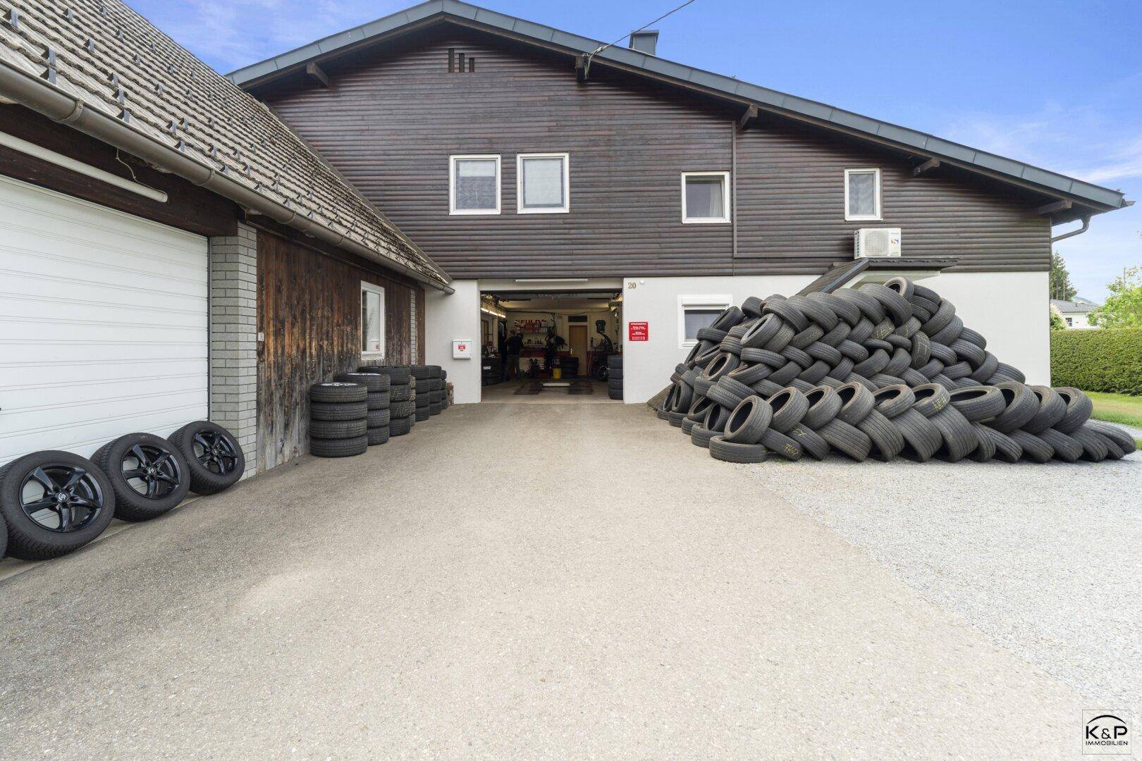 Außenansicht einer Werkstatt oder Garage mit vielen gestapelten Reifen und Zufahrt.