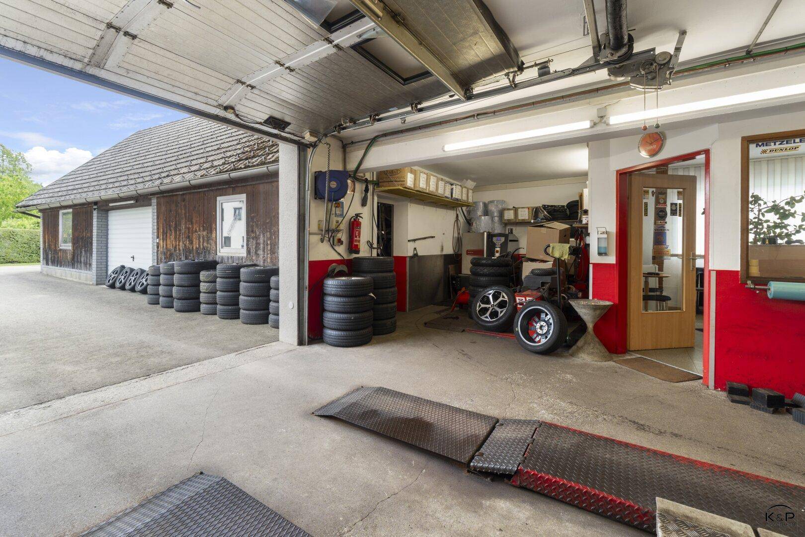 Innenansicht einer geräumigen Garage oder Werkstatt mit Hebebühne und vielen Reifen.