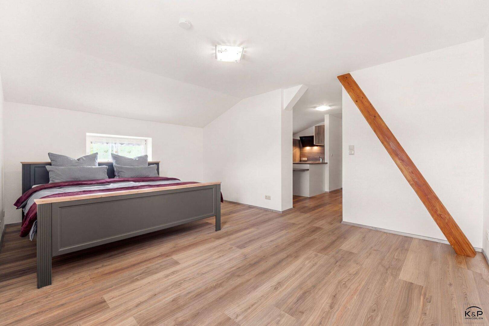 Schlafzimmer mit Laminatboden, Dachschräge und sichtbarem Holzbalken, angrenzend an die Küche.