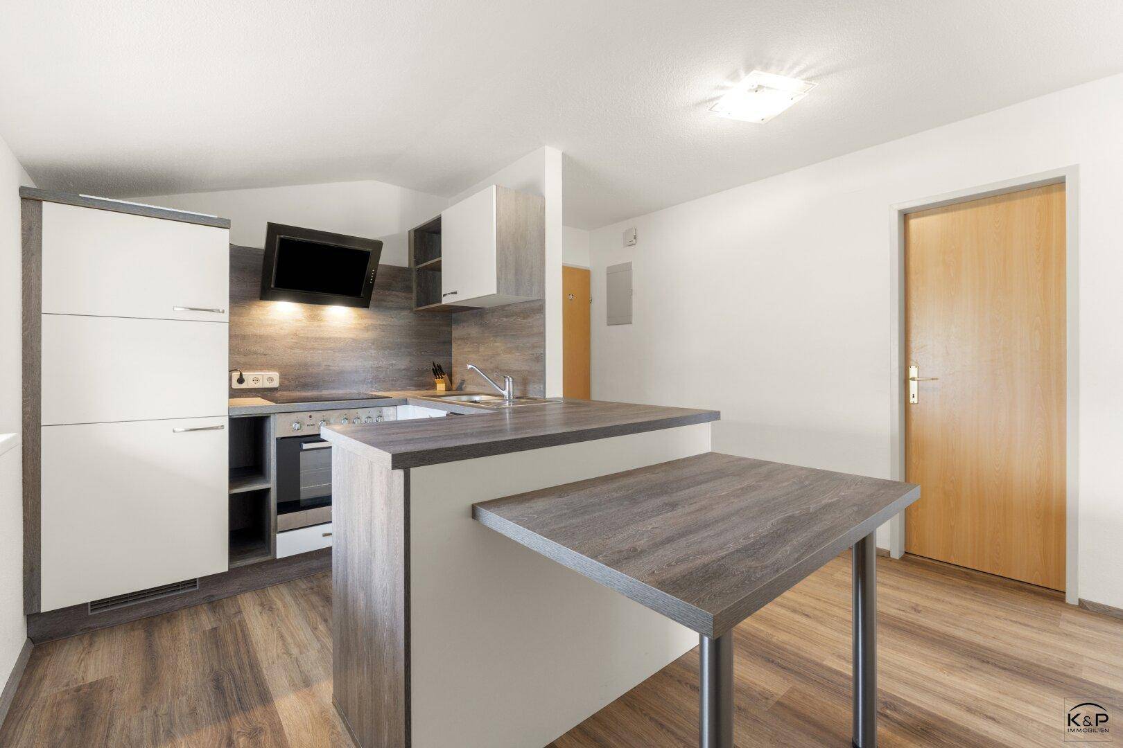 Moderne Küche mit weißen und grauen Schränken, integriertem Essbereich und Laminatboden.