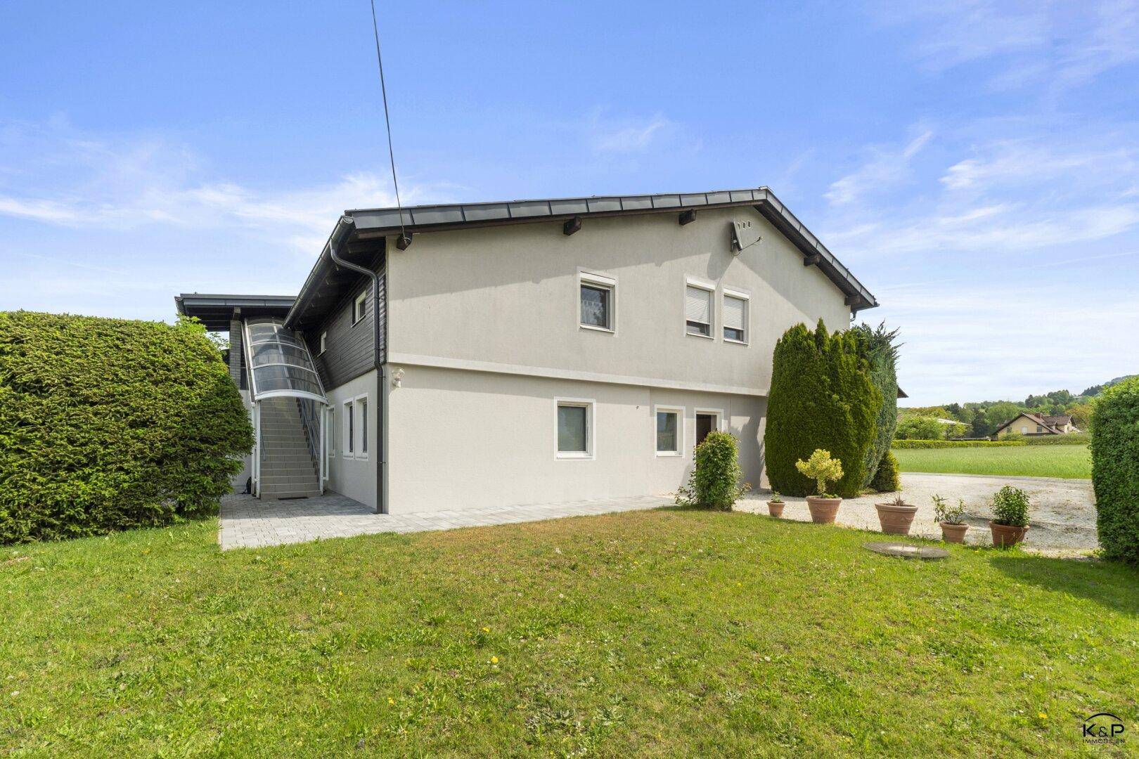 Seitenansicht des Hauses mit gepflegtem Rasen, einigen Topfpflanzen und einer Außentreppe.