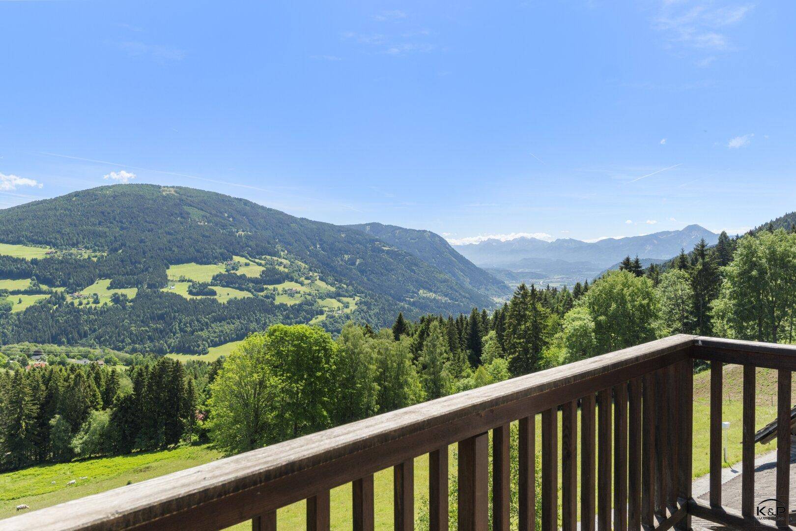 Holzbalkon mit weitem Blick über die grüne Hügellandschaft und die Berge.