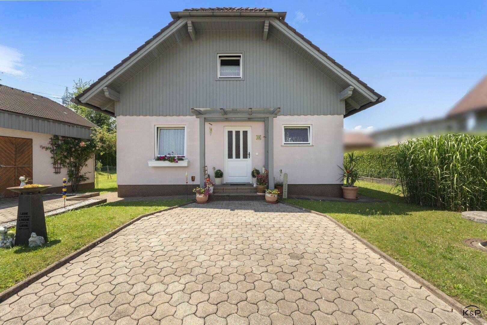 Frontansicht des Hauses mit Eingangsbereich, Blumenkästen und gepflasterter Zufahrt.