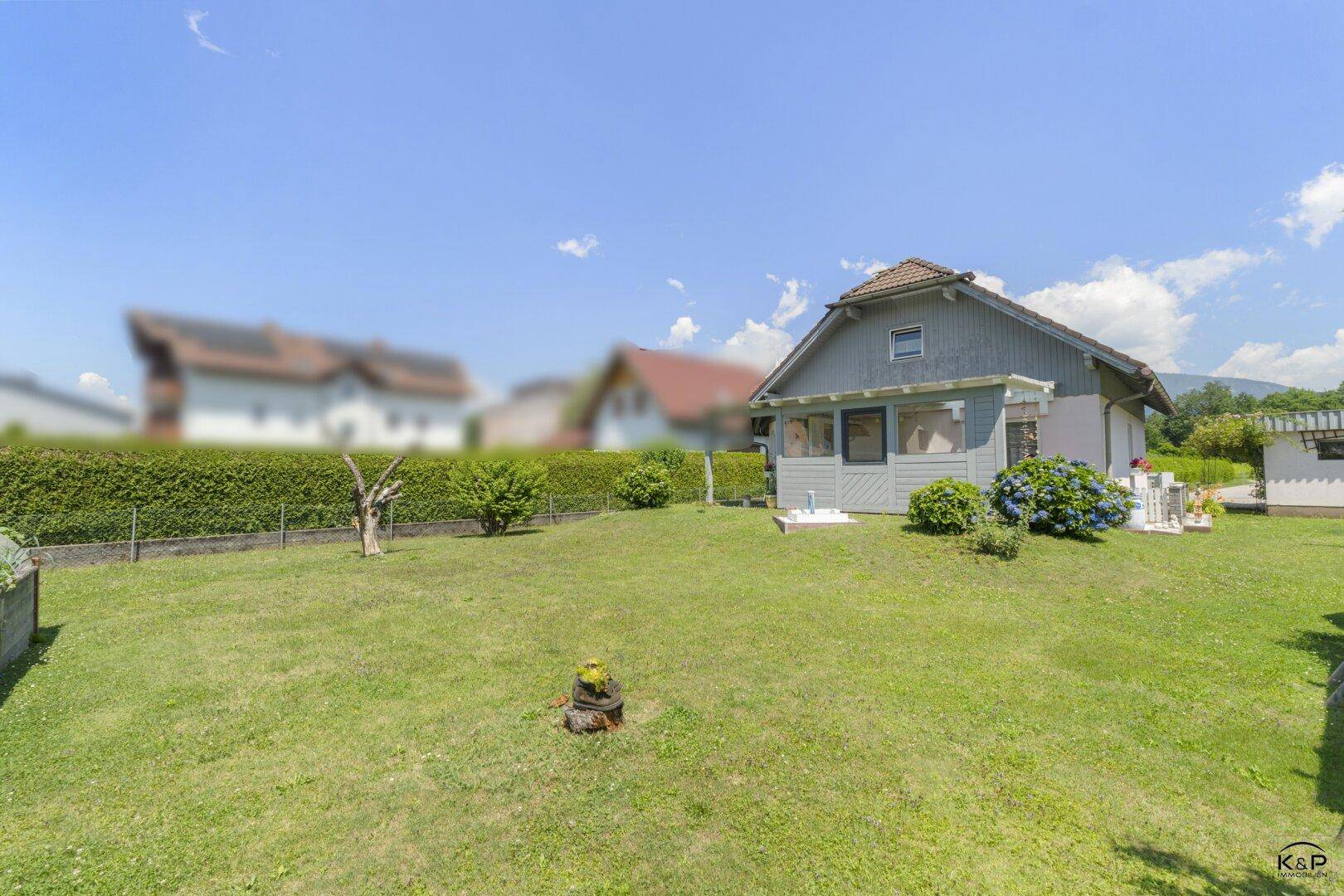 Weitläufiger grüner Garten mit Rasenfläche und dem Haus im Hintergrund unter blauem Himmel.