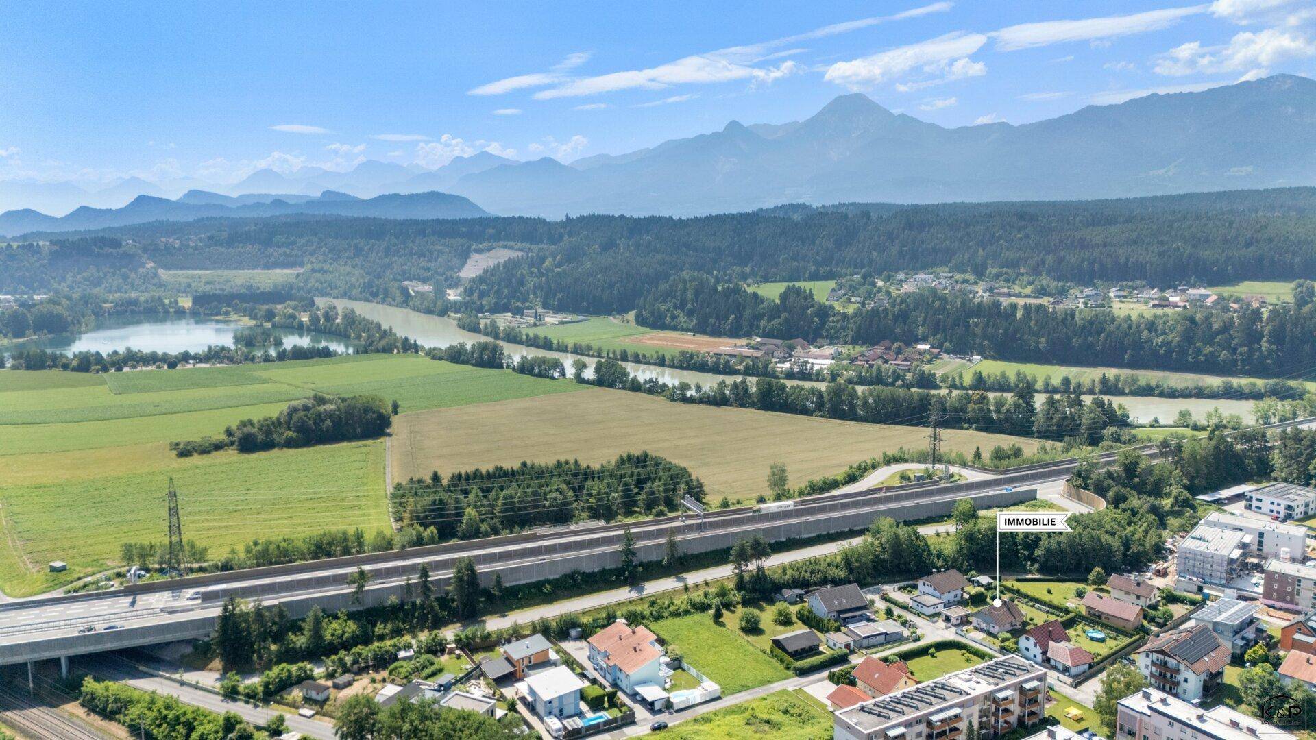 Luftaufnahme einer Wohngegend mit Fluss, Feldern und Bergen in der weiten Landschaft.