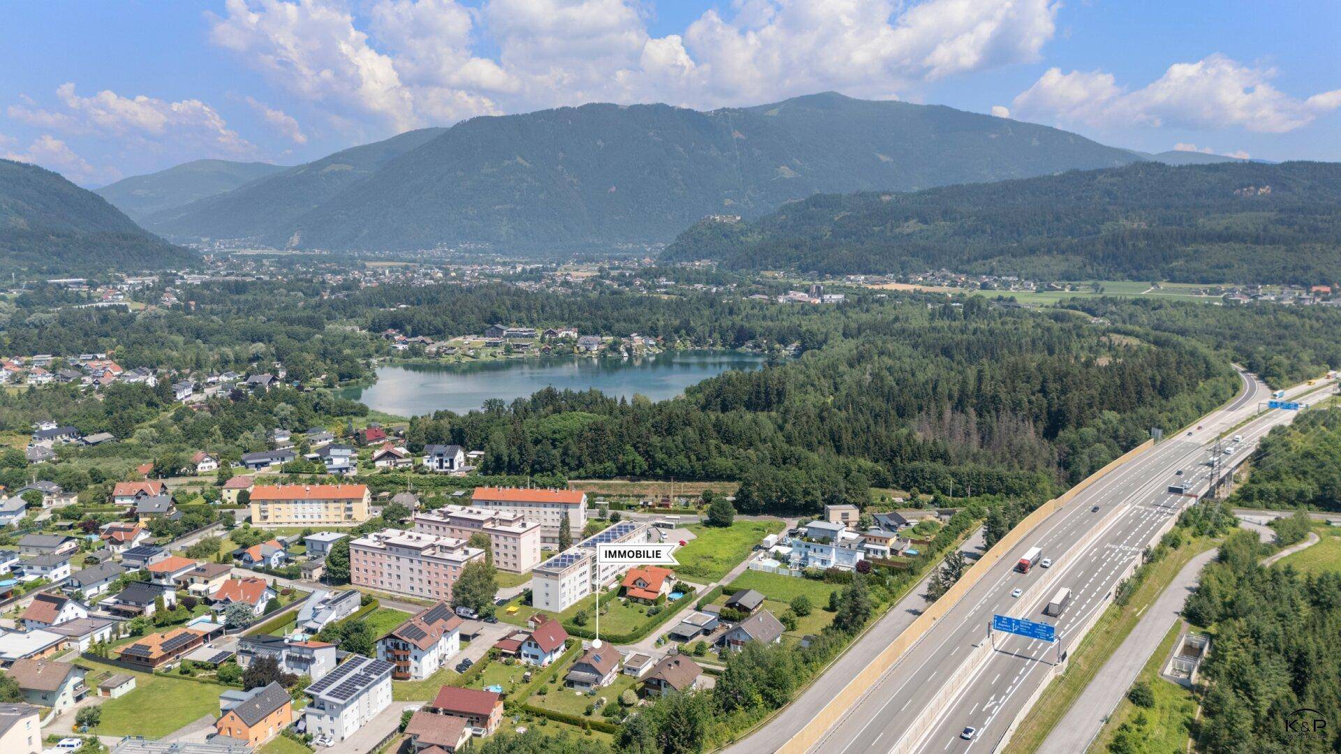 Panoramablick auf eine Stadt mit See, Autobahn und umliegenden Bergen.