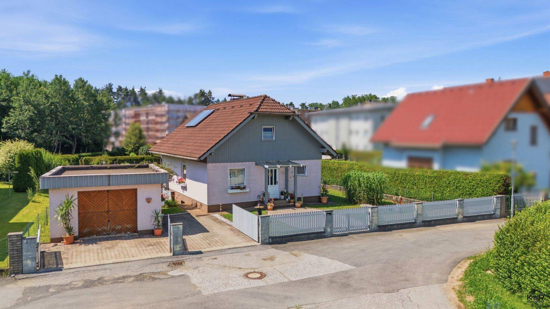 Luftaufnahme eines Einfamilienhauses mit Garage, umzäuntem Garten und gepflasterter Zufahrt.