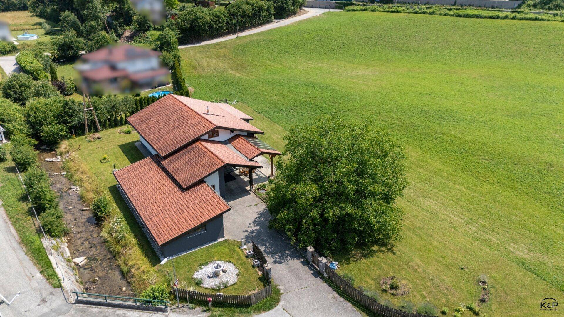 Vogelperspektive des Hauses mit Einfahrt, Vorgarten und weiten grünen Feldern.