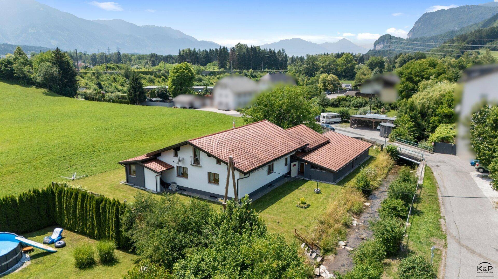 Haus mit rotem Ziegeldach, angrenzendem Bachlauf, Pool im Garten und Bergblick.