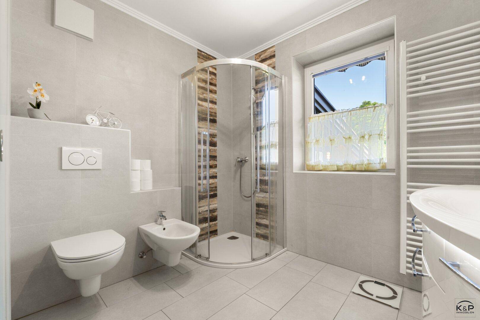 Modern gefliestes Badezimmer mit Duschkabine, WC, Bidet und beheiztem Handtuchhalter.