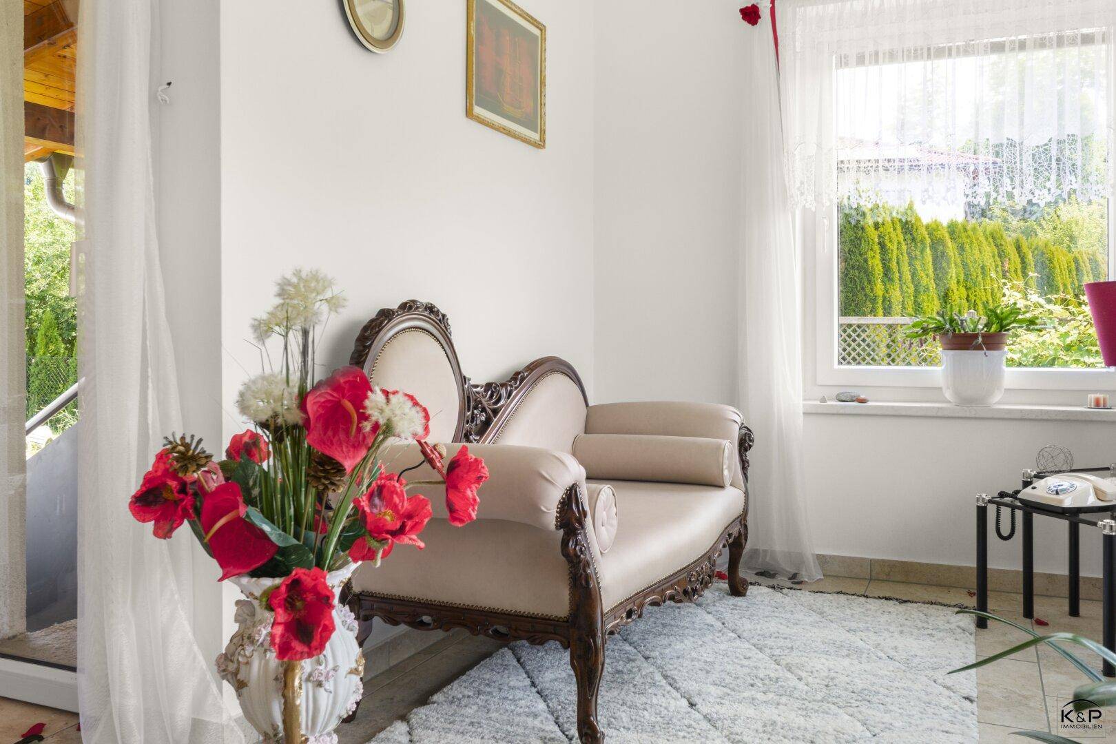 Heller Sitzbereich mit klassischer Chaiselongue, Teppich und Blick ins Grüne.