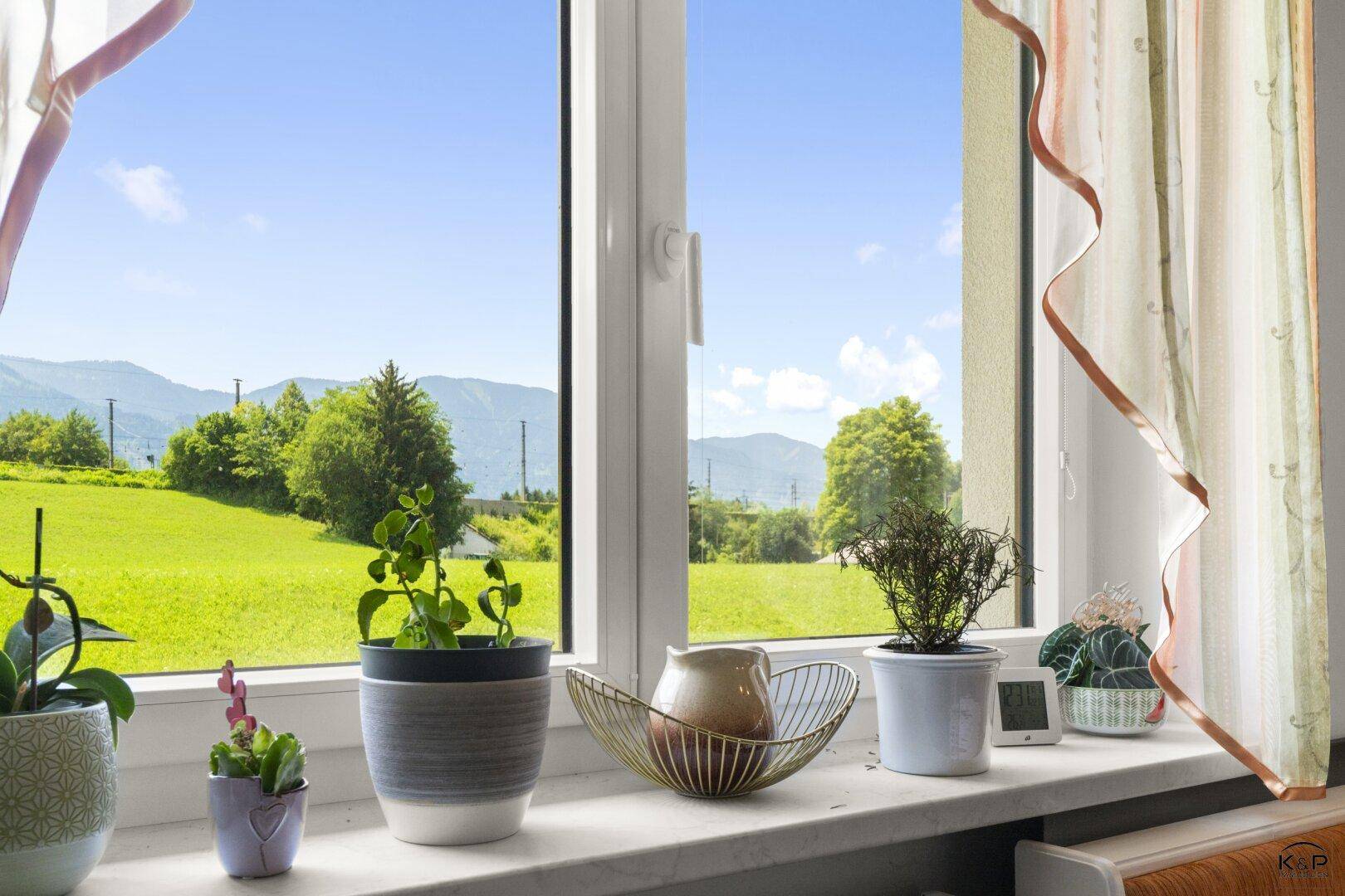 Fenster mit Blick auf grüne Wiesen und die umliegende Berglandschaft.