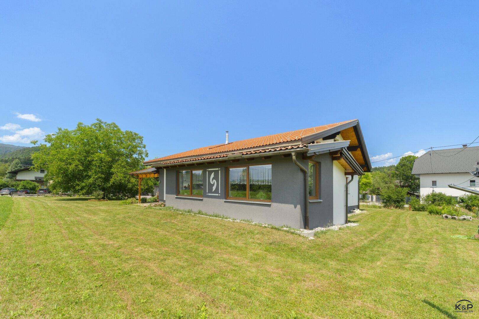 Seitenansicht des Hauses mit grauer Fassade, Fenstern und weitläufiger Rasenfläche.
