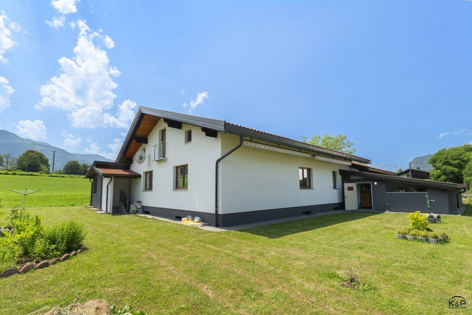 Rückansicht des Hauses mit kleinem Balkon, grüner Rasenfläche und Bergblick.
