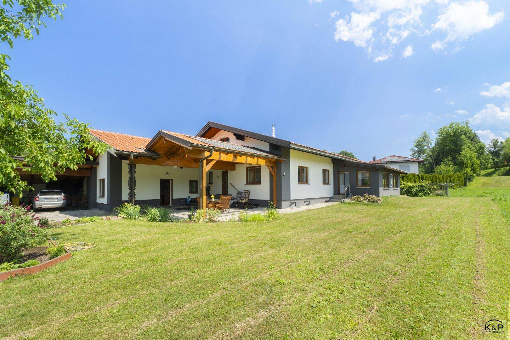 Haus mit rotem Ziegeldach, großer Rasenfläche und überdachter Terrasse mit Solarpaneelen.