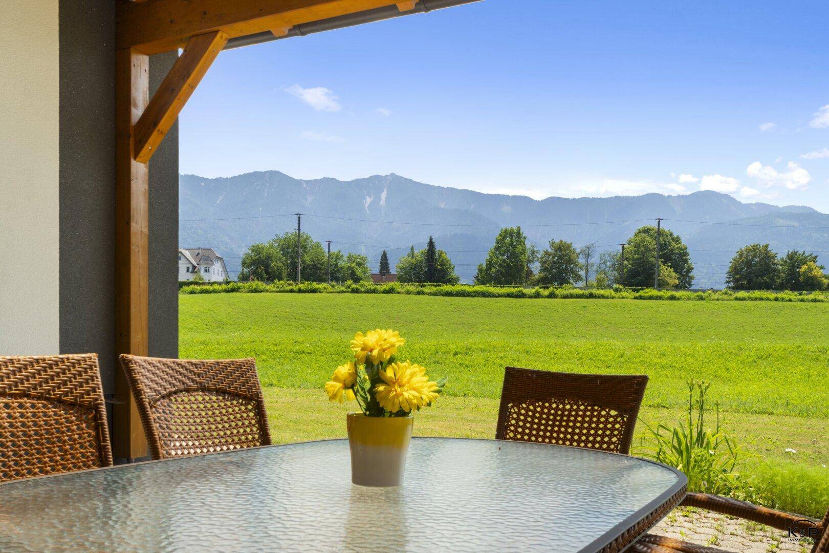Gemütliche Terrasse mit Korbmöbeln und einem weiten Blick über grüne Felder und Berge.