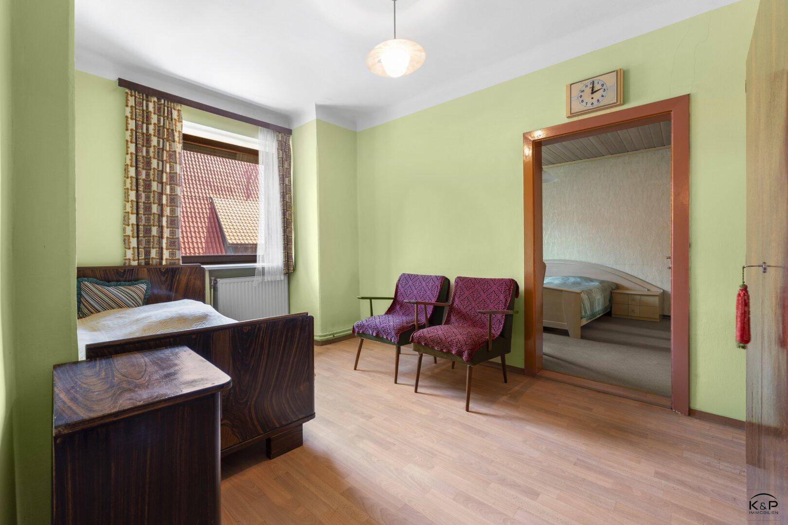 Gemütliches Schlafzimmer mit Holzfußboden, hellgrünen Wänden und Zugang zu einem weiteren Schlafzimmer.