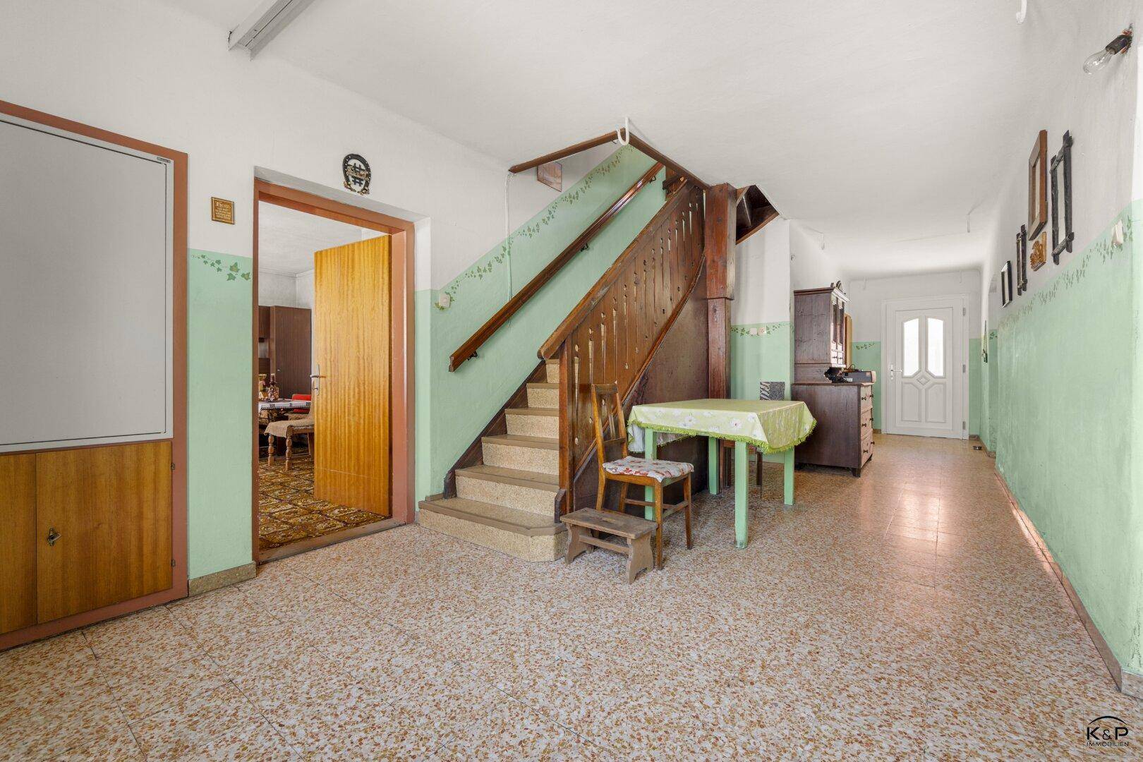 Geräumiger Flur mit einer traditionellen Holztreppe und Terrazzoboden im Altbau-Stil.