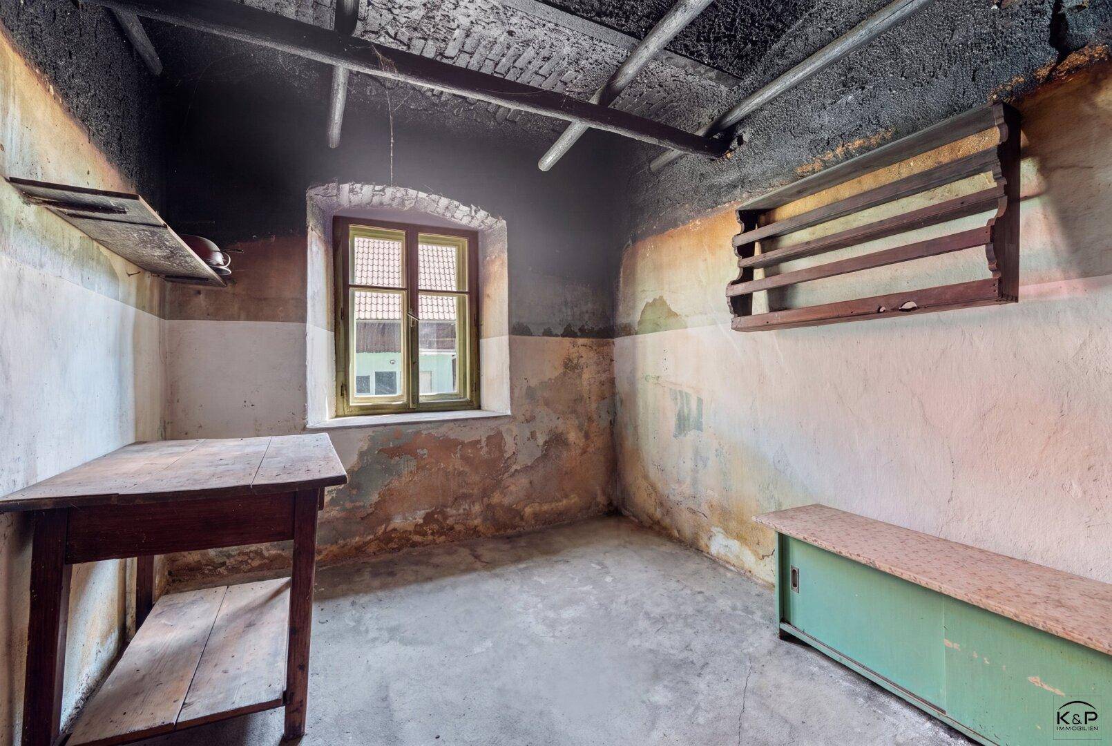 Rustikaler Abstellraum mit einfacher Einrichtung, kleinem Fenster und sichtbaren Gebrauchsspuren.
