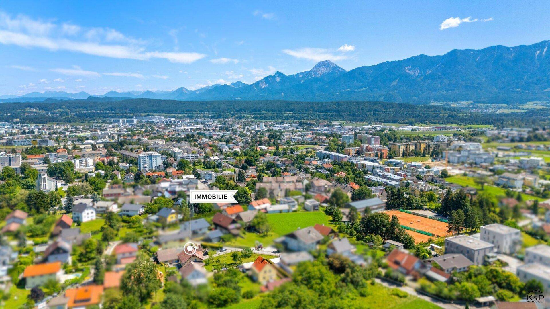 Panoramische Luftaufnahme einer Stadt mit Bergen im Hintergrund, die Immobilie ist deutlich markiert.