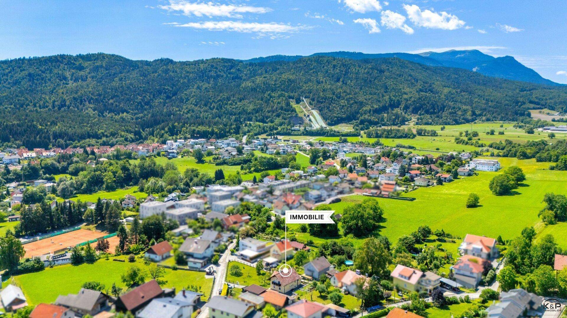 Weitläufige Luftaufnahme einer Wohngegend mit Bergen im Hintergrund und Tennisplätzen in der Nähe.