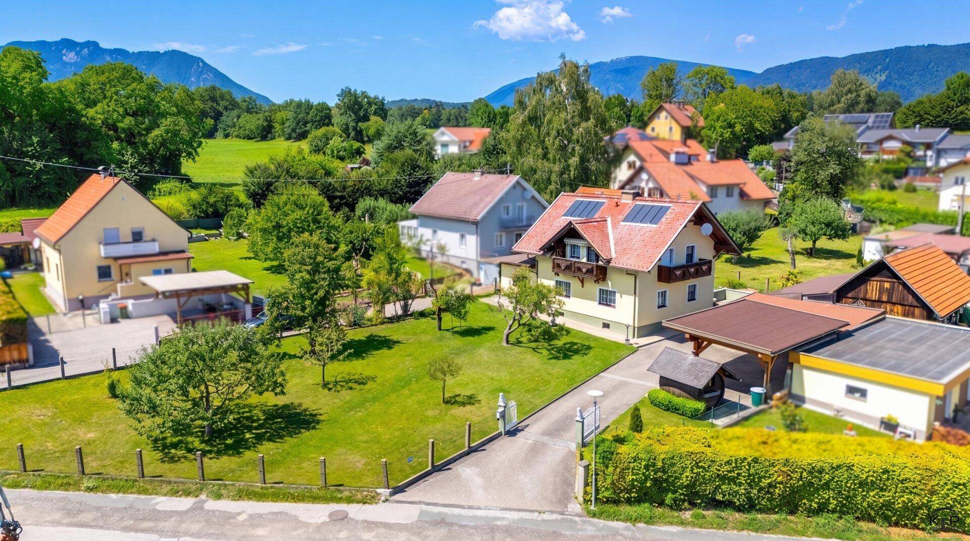 Vogelperspektive eines Einfamilienhauses mit großem Garten, umgeben von weiteren Wohnhäusern und grüner Landschaft.
