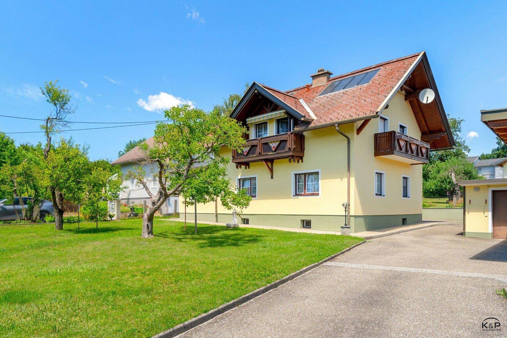 Seitenansicht des Hauses mit gelber Fassade, Satteldach, Balkon und Photovoltaikanlage auf dem Dach.