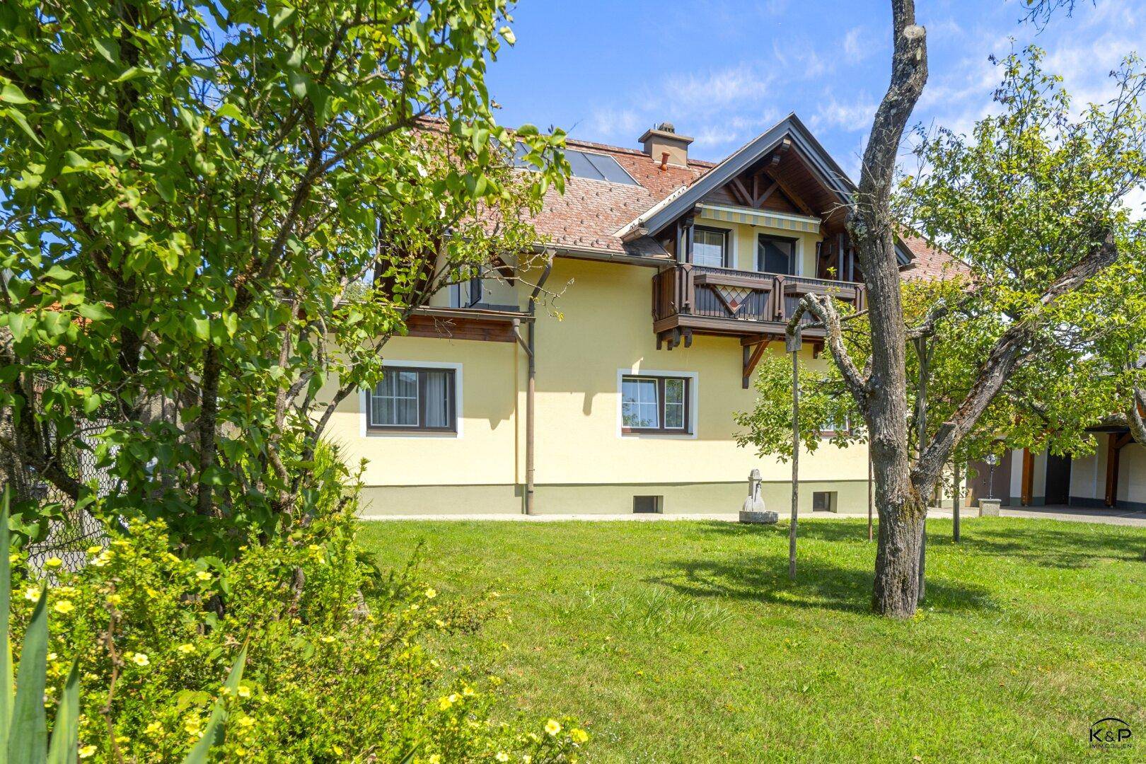Das Einfamilienhaus, umgeben von üppigem Grün und blühenden Sträuchern im sonnigen Garten.