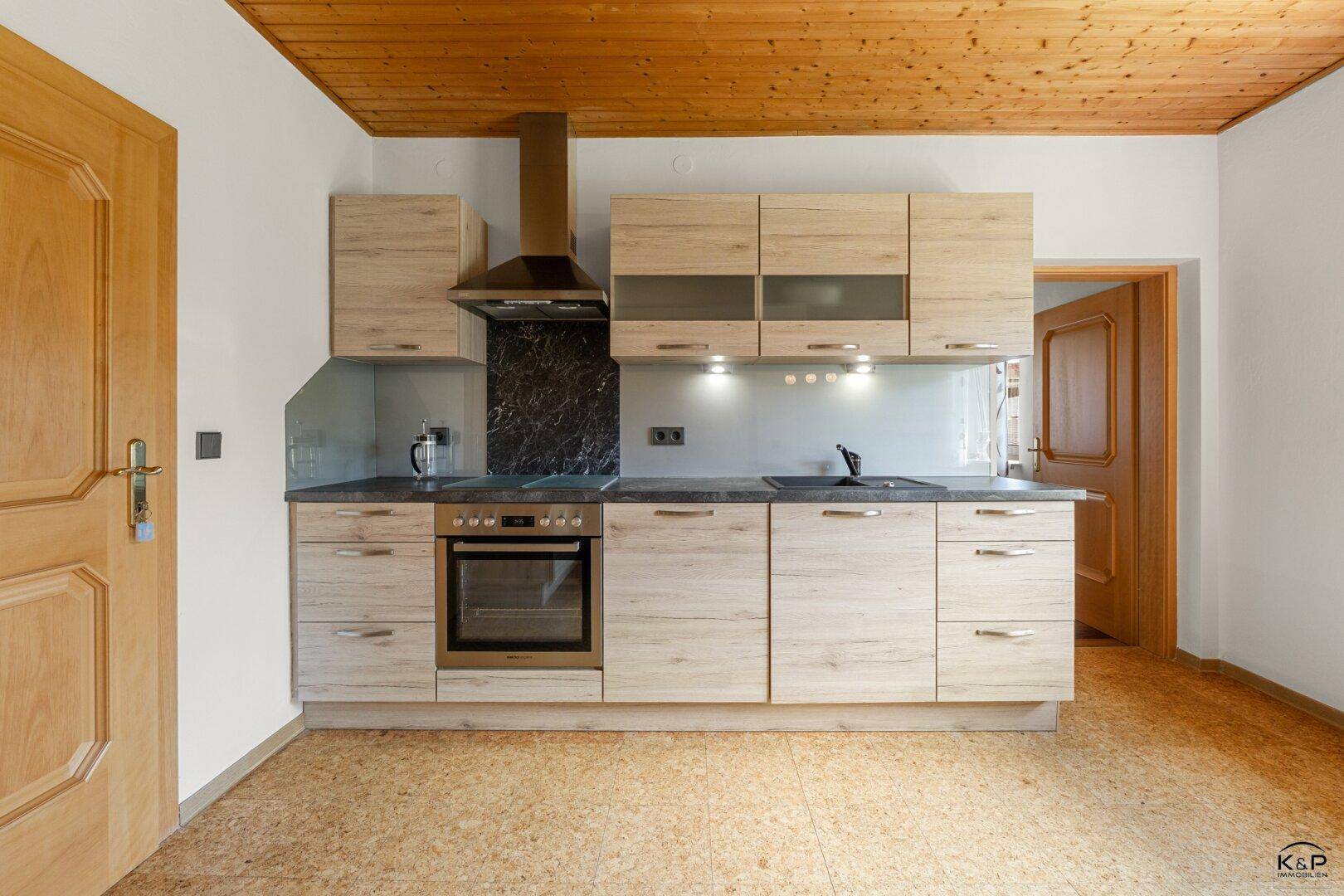 Funktionale Küche mit hellen Holzschränken, Einbauherd und Dunstabzugshaube, ausgestattet mit Korkboden.