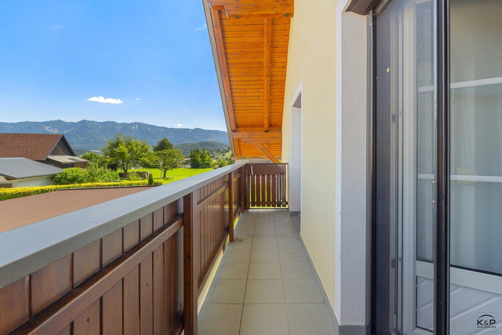 Geräumiger Balkon mit Holzboden und Fliesen, bietet einen weiten Blick auf die umliegende Landschaft und Berge.