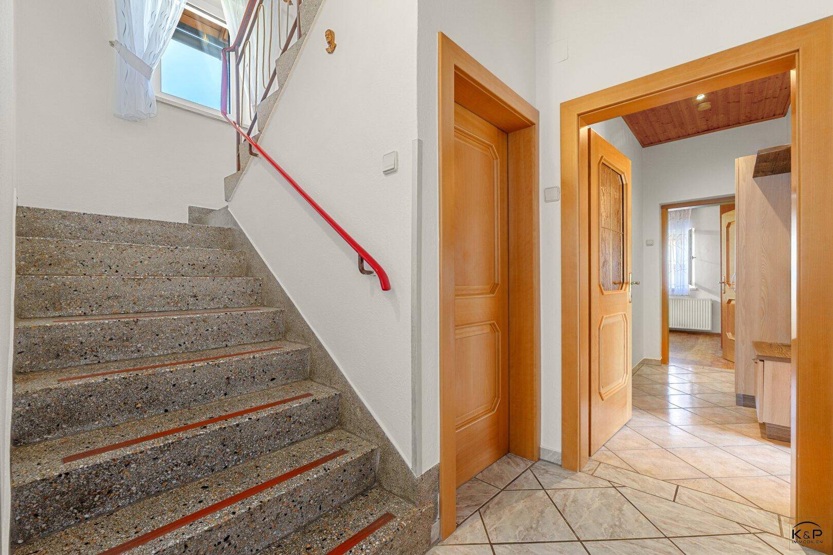 Heller Flur mit Steintreppe, Holzgeländer und gefliestem Boden, führt zu weiteren Räumen.