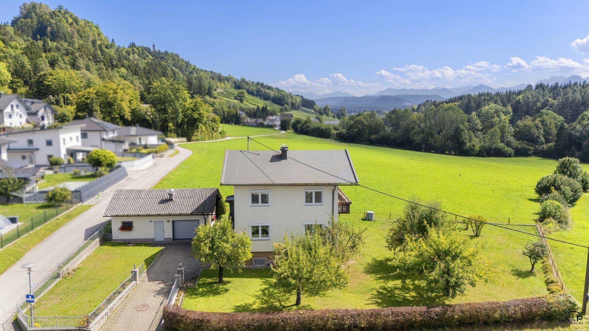Seitenansicht des Hauses mit großem Garten und Blick auf die umliegenden grünen Hügel und Berge.