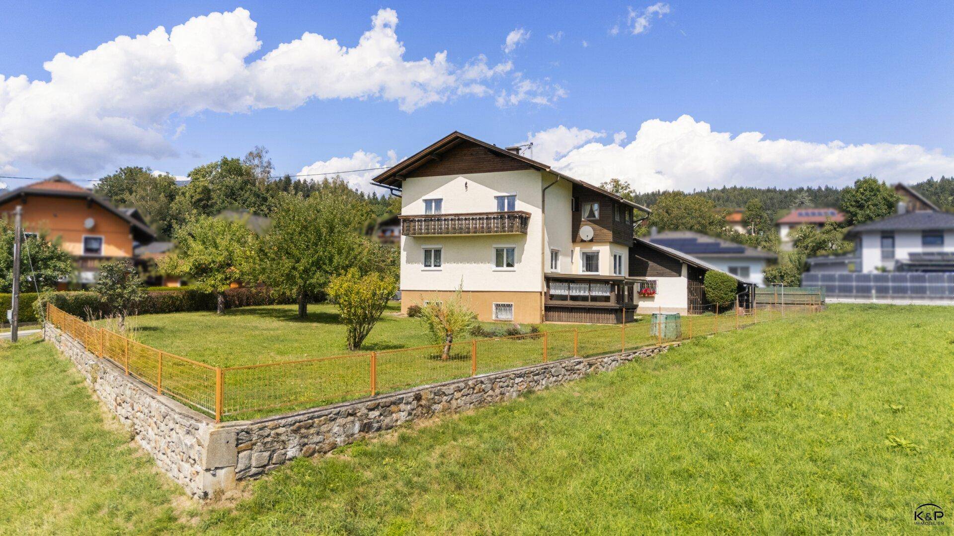 Seitenansicht des Hauses mit kleinem Balkon und einem umzäunten Gartenbereich in sonniger Lage.
