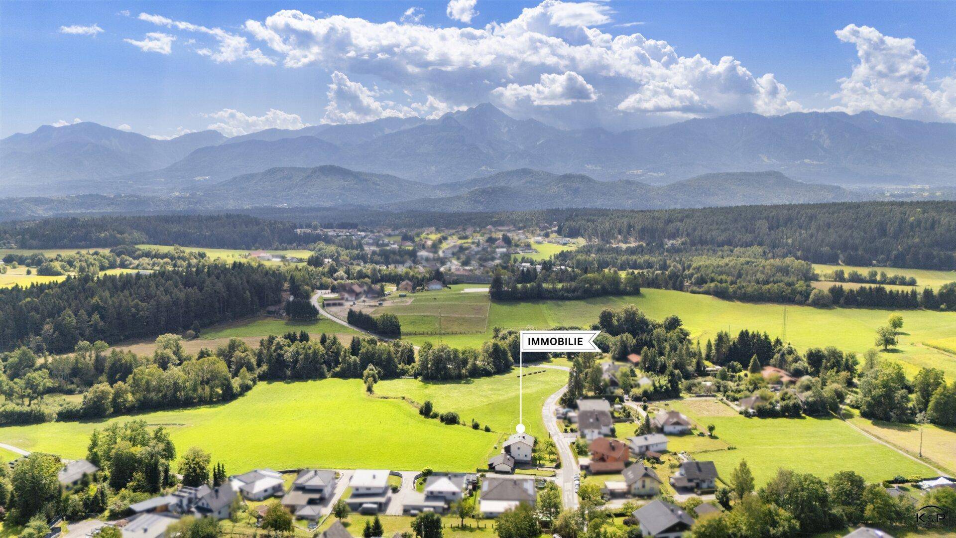 Weitläufige Luftaufnahme der Immobilie, eingebettet in eine grüne Landschaft mit Bergen am Horizont.