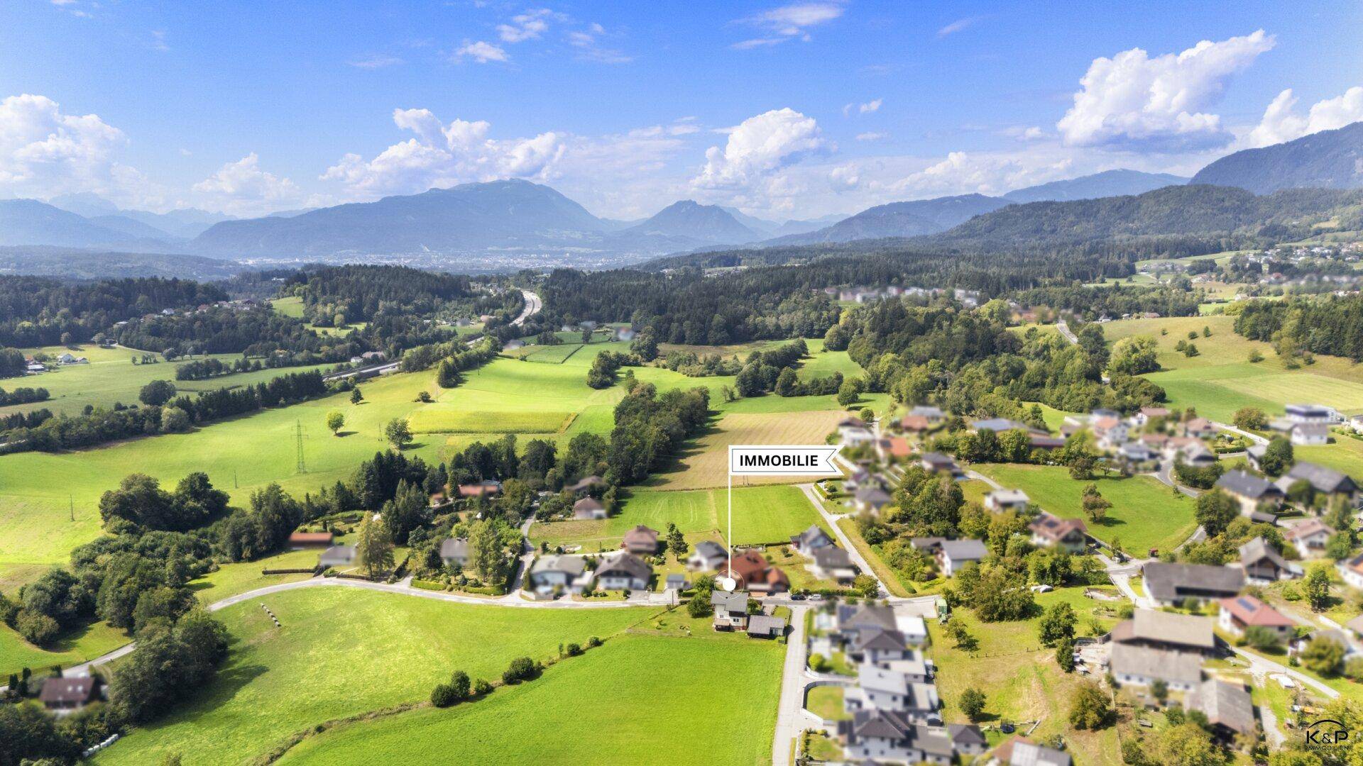 Panoramische Luftaufnahme der Immobilie in einer weitläufigen Landschaft mit Bergen und Autobahn im Hintergrund.