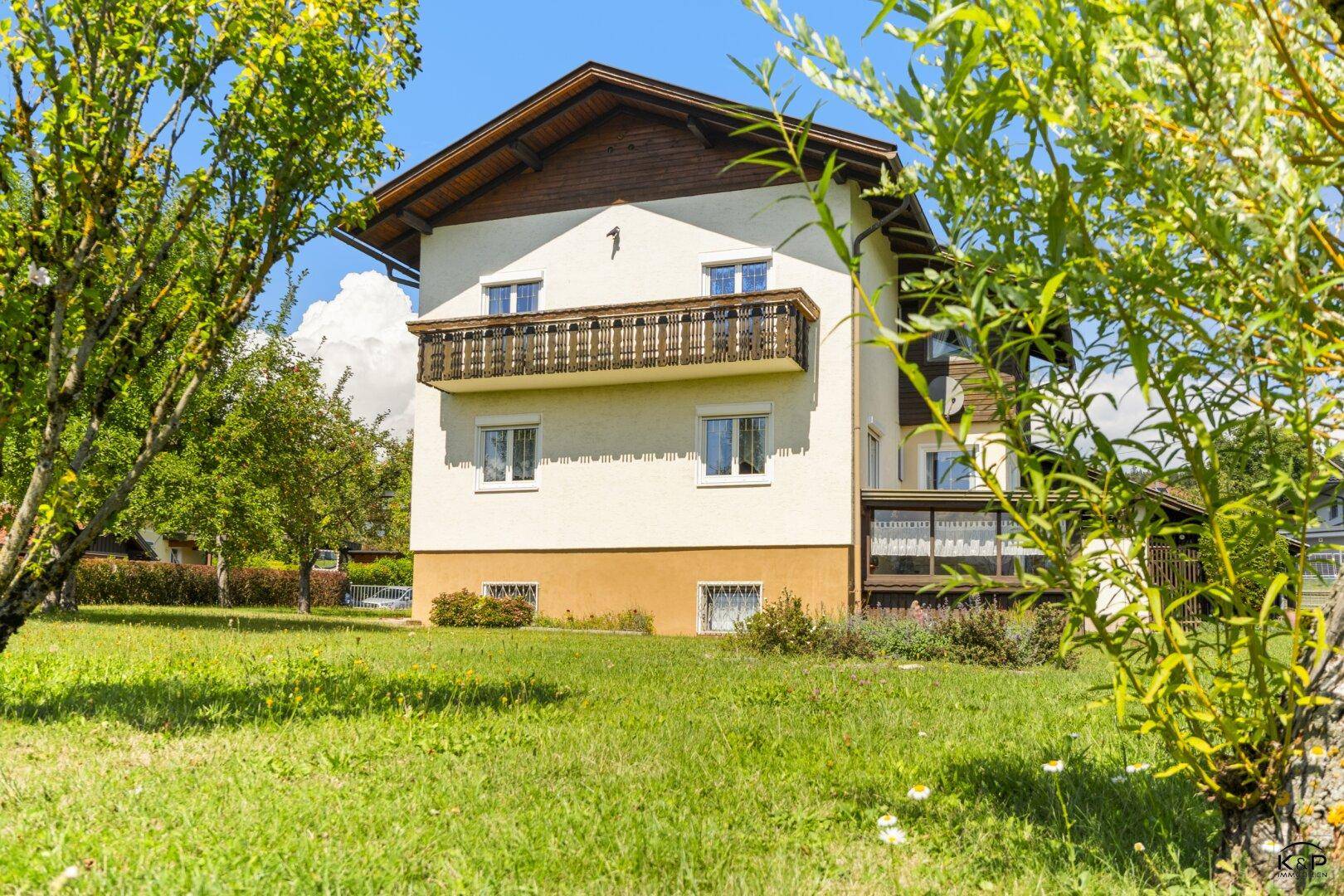 Ansicht des Hauses vom grünen Garten aus, mit einem traditionellen Holzbalkon und viel Rasenfläche.