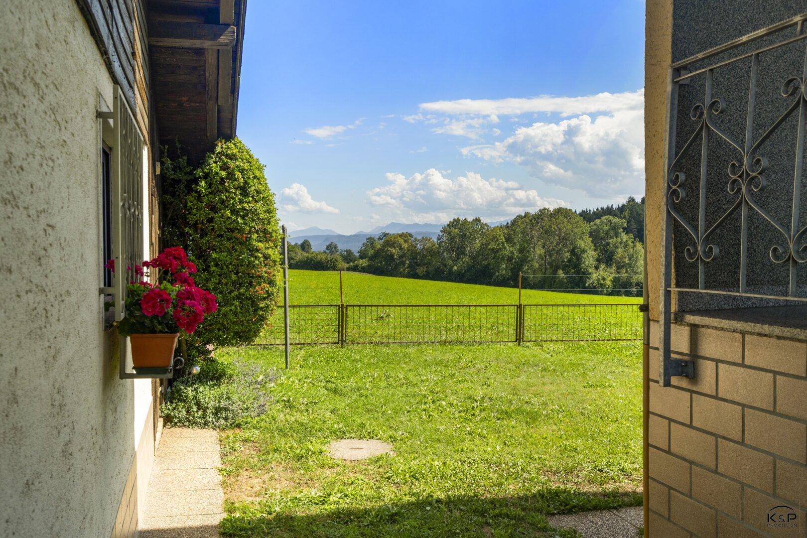 Blick von der Terrasse oder dem Eingangsbereich auf eine weite grüne Wiese und die Berge.
